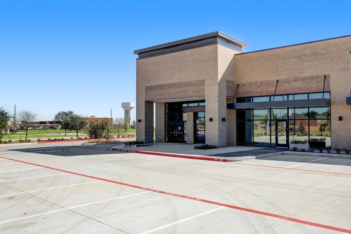 Side angle of a brick and glass commercial building with landscaped greenery and parking in Houston, TX