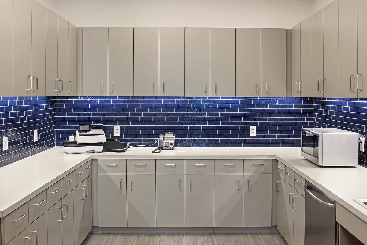 Bright and functional office kitchenette with gray cabinets and blue subway tile backsplash, designed by GSD Construction in Houston, TX