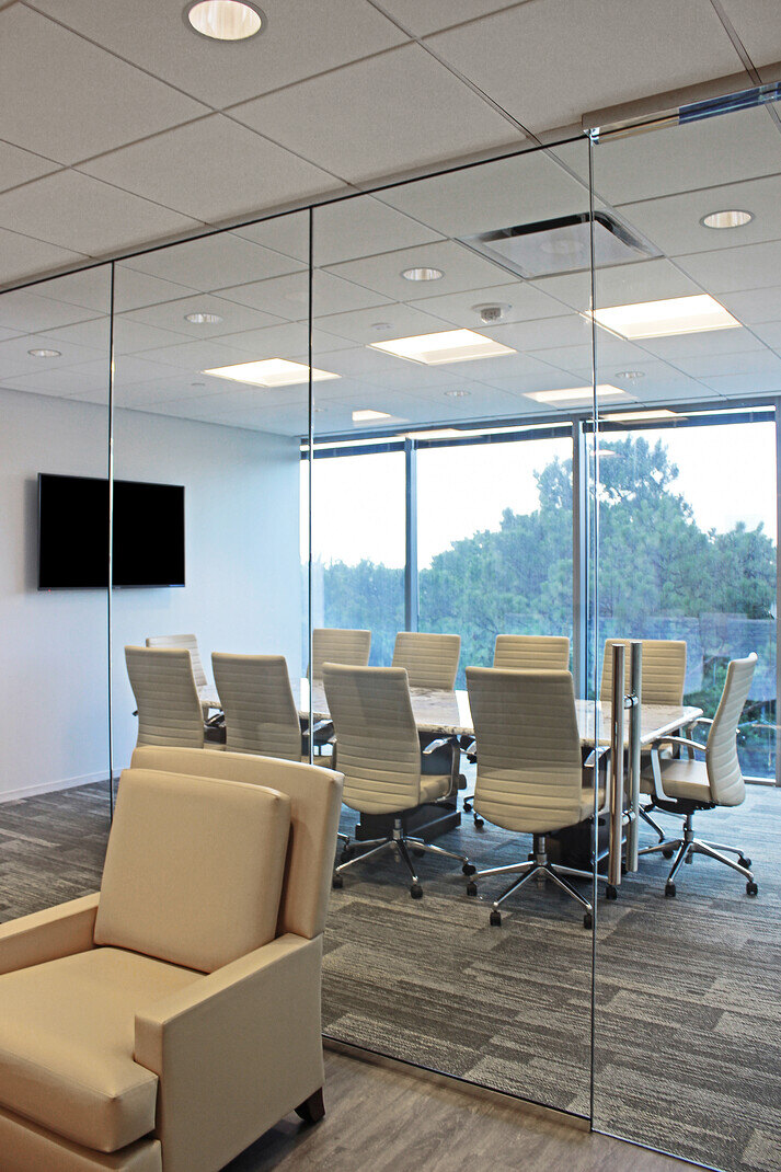 Bright and modern conference room with glass walls, white chairs, and a view of the outdoors in a Houston, TX renovation by GSD Construction